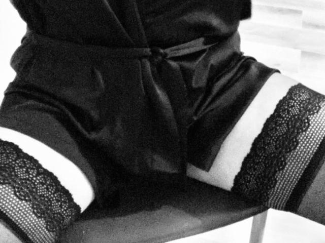 Le short en satin noir d'EstrelaFrenchie, avec des bas hauts en dentelle, expose ses fesses galbées et ses cuisses. Le short est noué à la taille. Photo en noir et blanc..