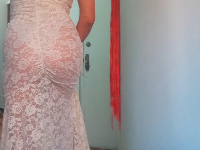 CoupleMature's white lace dress, showing her ass, is sheer with floral patterns, hanging her up against a door with a red scarf on the right.