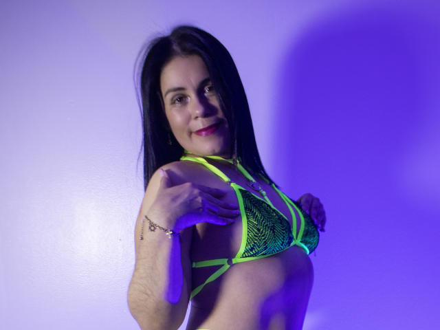 GirasolWalton with black hair, green neon mesh bikini, small tits, smiling, hands on chest, purple light, bracelet on left wrist, light skin, pink lipstick, confident, sexy.