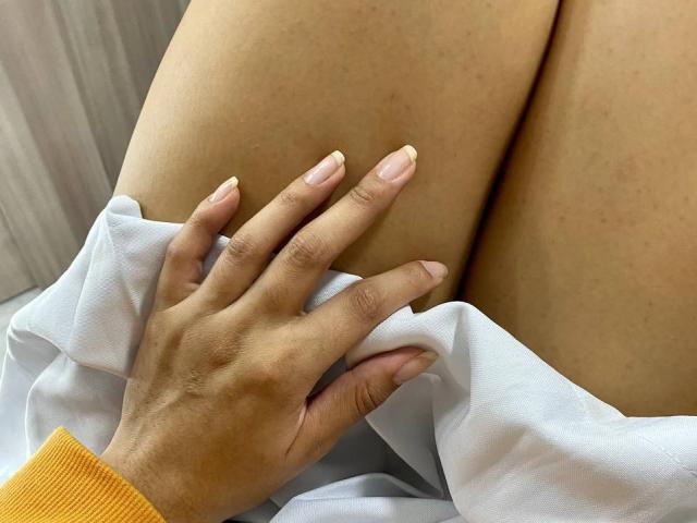 JessicaSoler's hand with pale pink nails rests on her bare thigh, showing her tan skin. She's wearing a white shirt with an orange sleeve.