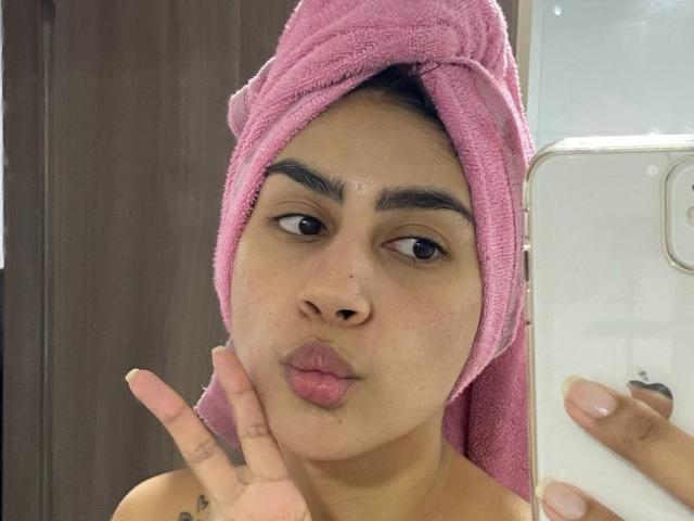 JessicaSoler with pink towel on head, pouty lips, brown eyes, and nose ring, making a peace sign with phone in mirror selfie, showing a tattoo on her hand.