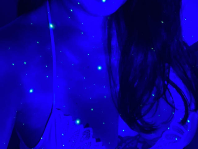 EstrelaFrenchie's glowing blue tits, with small green lights scattered across her chest, and long dark hair flowing to the right. The image has a strong blue light effect.