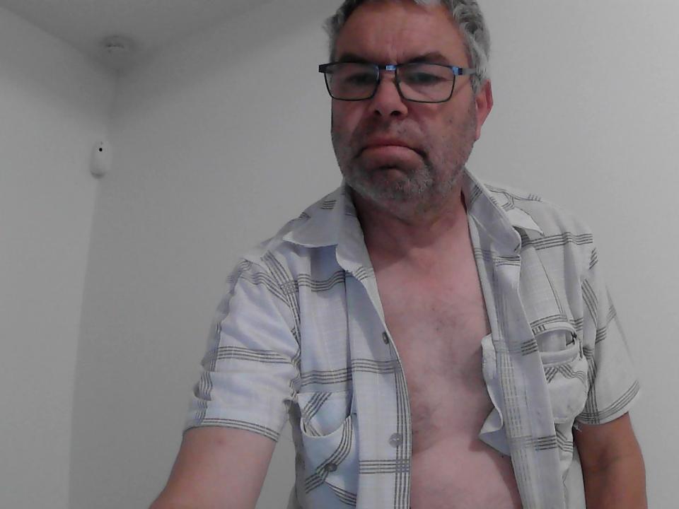 Un Jedi di mezza età con capelli grigi, occhiali e barba, che indossa una camicia bianca a quadri aperta, che lascia scoperto il petto e l'addome. La sua camicia è sbottonata, mostrando il suo petto nudo..