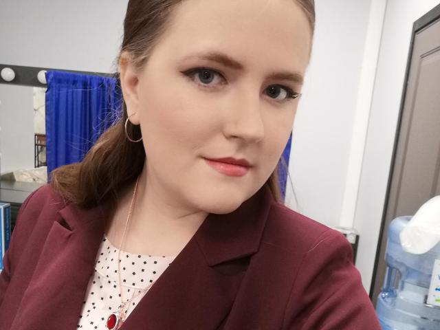 Melissa, con la pelle chiara, i capelli castani raccolti in una coda di cavallo, indossa un blazer color borgogna, una camicia bianca a pois, rossetto rosa e orecchini a cerchio dorati, e ha un'espressione carina e sicura di sé..