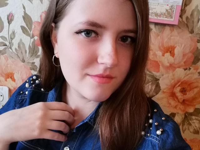 Melissa, con lunghi capelli castani, occhi azzurri, indossa una camicia di jeans blu con bottoni di perle, un leggero sorriso, tiene il colletto, piccoli orecchini a cerchio, labbra rosa chiaro, pelle chiara..