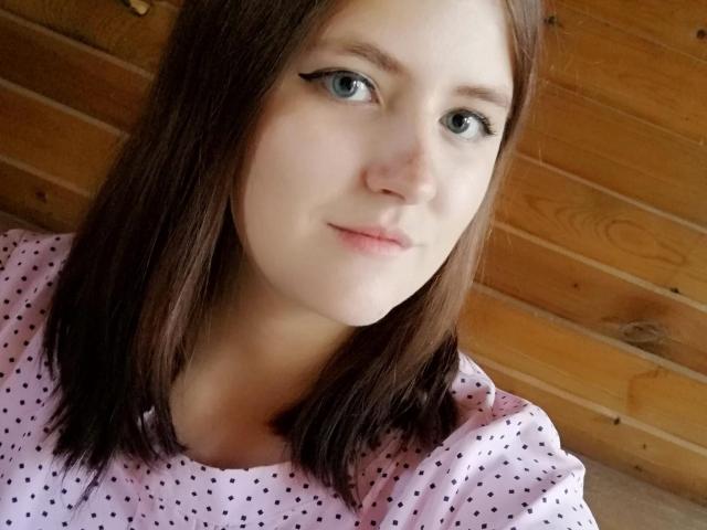 MelissaFine ha la pelle chiara, gli occhi azzurri e i capelli castani lunghi fino alle spalle. Indossa una camicia rosa a pois, con eyeliner nero e un sorriso appena accennato. Sfondo con pannelli di legno..