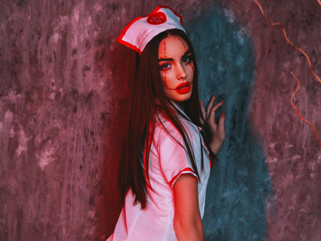 MelisaWiesel with long brown hair, wearing a white nurse hat and red lipstick, has stitches on her face, looking back with red lighting, in a tight white nurse dress.