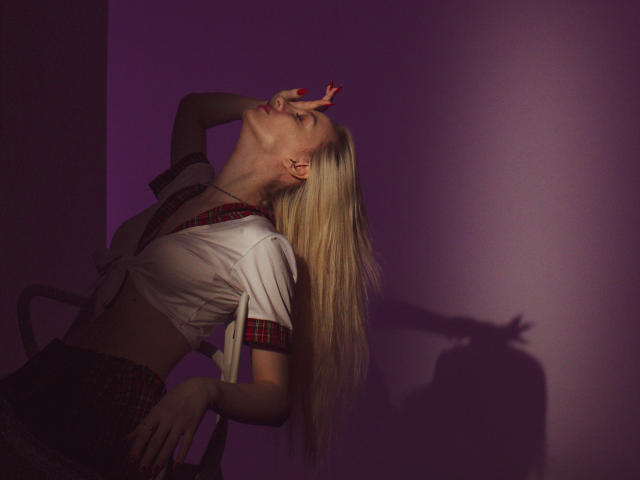 LexyGlam, blonde with long hair, leans back, eyes closed, hand on head, wearing a white shirt and plaid skirt, shadow on wall, purple light, sexy pose.