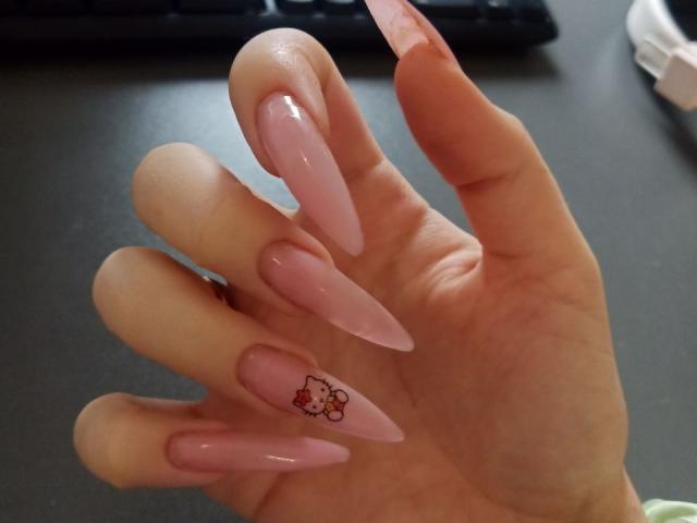 La main de Zanoza, avec des ongles roses très longs et brillants, et un petit tatouage de fleur sur l'ongle du petit doigt. Sans seins, sans fesses, sans vulva, juste des ongles..