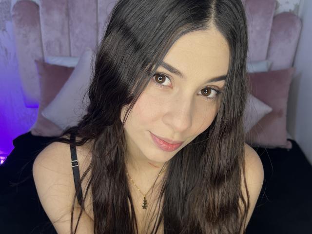 NikoleFoster has long, dark brown hair, brown eyes, and a subtle smile. She's wearing a black strap top, showing her bare shoulders and a small necklace.