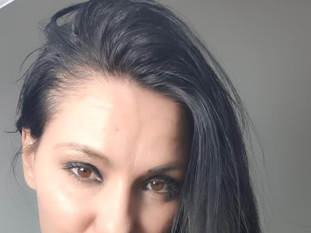 JoliDanielle's face with straight black hair, brown eyes, and slight forehead blemish. She's looking directly at the camera with a neutral expression. Her skin is fair.