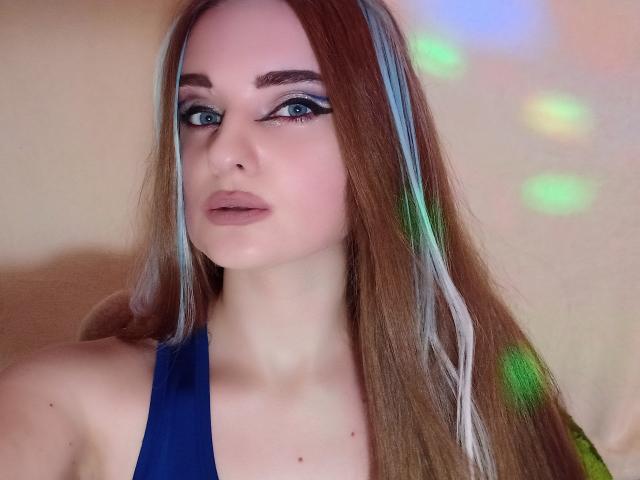 KariMillie heeft lang bruin haar met blauwe highlights, draagt een blauwe top, heeft dramatische zwarte eyeliner en blauwe ogen, en een subtiele roze lipstick. Haar borsten zijn klein..