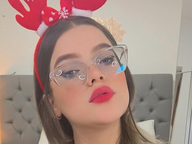 KimSummer with red reindeer antlers, clear glasses, and pink lips, looking up, has brown hair and a slight tan, wearing a white shirt, showing her nose.