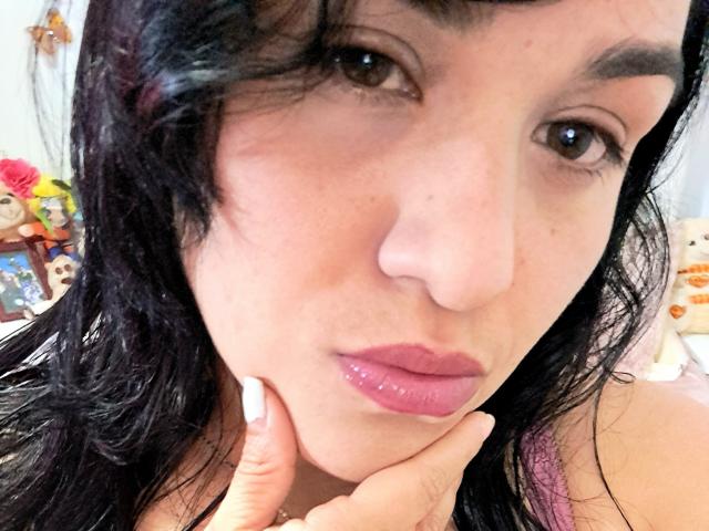 VivianaThomson has dark wet hair, brown eyes, and glossy pink lips, with her finger touching her chin. Her pink nipples are visible under a pink top.