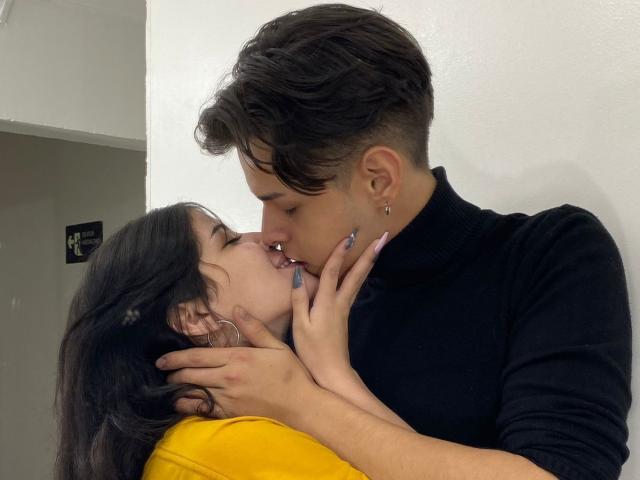JadeAndLeo, avec ses cheveux courts et foncés et son pull noir, embrasse une autre JadeAndLeo, qui a les cheveux longs et noirs et porte une chemise jaune, en tenant doucement son visage..