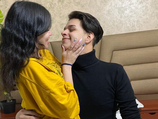 JadeAndLeo met lang zwart haar in een geel shirt, die Leo's gezicht vasthoudt met haar hand, waarbij haar geverfde nagels te zien zijn, en die glimlachend naar Leo kijkt, die een zwarte coltrui draagt..