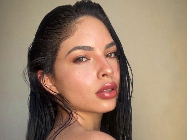 LolaHeaven heeft nat zwart haar, bruine ogen en glanzende, roze lippen. Ze kijkt over haar schouder met een sexy, zelfverzekerde uitdrukking. Haar huid is licht en glad..