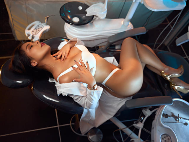 MeganWisse, Asian woman, laying in a dental chair, white bra and panties, open shirt, gold heels, eyes closed, hand on tits, other hand on ass, relaxed, sexy.