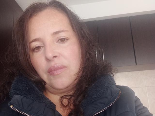 CandHoney hat volle Lippen, braunes, welliges Haar und trägt eine dunkelblaue, gepolsterte Jacke mit einem Fleece-Kragen. Ihre braunen Augen schauen leicht zur Seite..