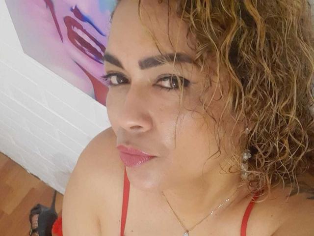 SolmaryHot has curly brown hair, red lipstick, and wears a red top with thin straps. She's looking up with a slight pout, showing her cute face and small tits.