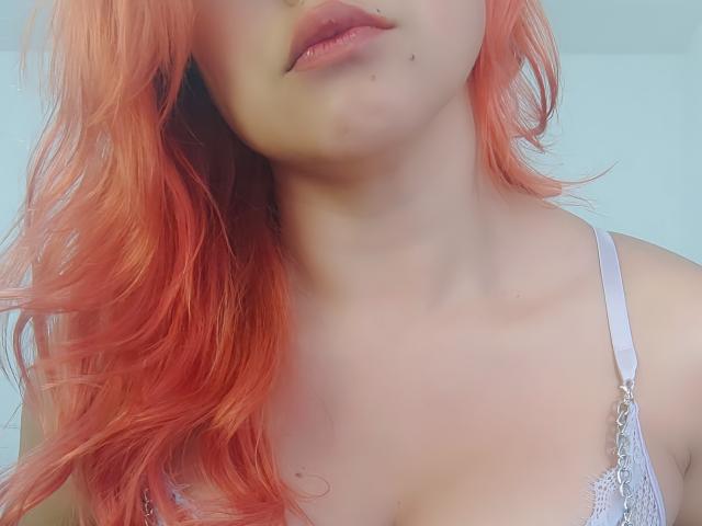 AhriValvet con capelli rosa, pelle chiara, piccole lentiggini sul mento, indossa un reggiseno di pizzo bianco, scollatura visibile, labbra rosa tenue, parte superiore del torace in primo piano, primo piano con la testa leggermente inclinata..