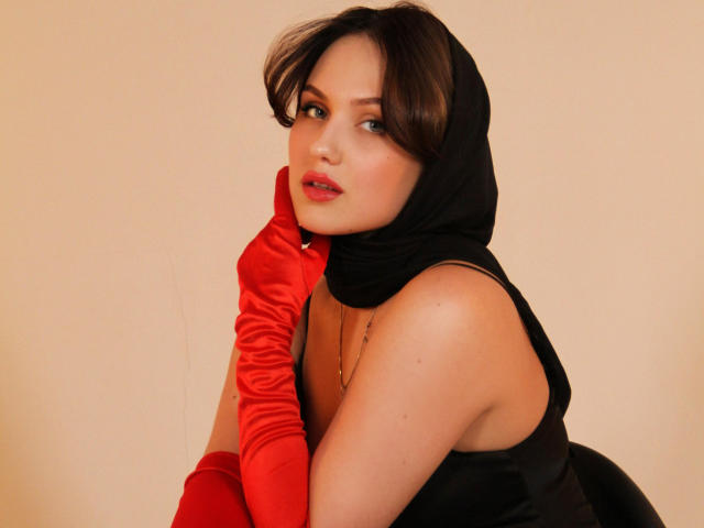 Lisa Francis, con i capelli scuri, indossa un foulard nero e guanti di raso rosso, mentre si guarda indietro, mostrando le spalle scoperte e la parte superiore del petto, con un sorriso appena accennato sul viso..