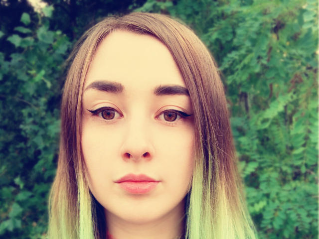 HentaiShing69 hat hellbraune Augen, glattes, braunes Haar mit grünen Spitzen und blickt mit einem neutralen Ausdruck. Ihr Make-up umfasst einen Eyeliner mit Flügel. Sie hat kleine, rosafarbene Lippen..
