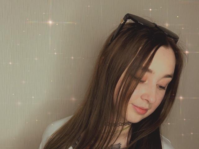 HentaiShing69 ha lunghi capelli castani, indossa degli occhiali da sole sulla testa, una collana nera e un sorriso appena accennato con gli occhi chiusi. È una ragazza carina con un piccolo tatuaggio..