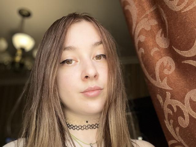 HentaiShing69 has light brown hair, yellow eyes, and a small black choker with a pendant. She's looking to the side with a slight smile. Her tits are small.