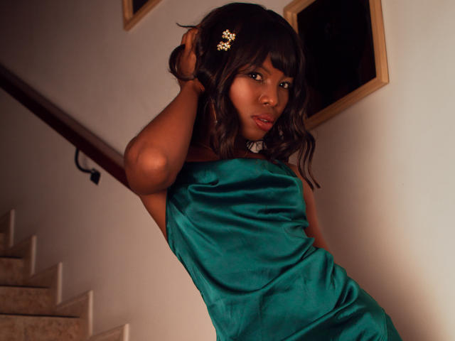 Michelle Flores, avec ses cheveux bruns foncés, portant une robe en satin vert, a une pince à cheveux en forme de fleur, regarde l'appareil photo, une main dans les cheveux, debout sur les marches, sexy..