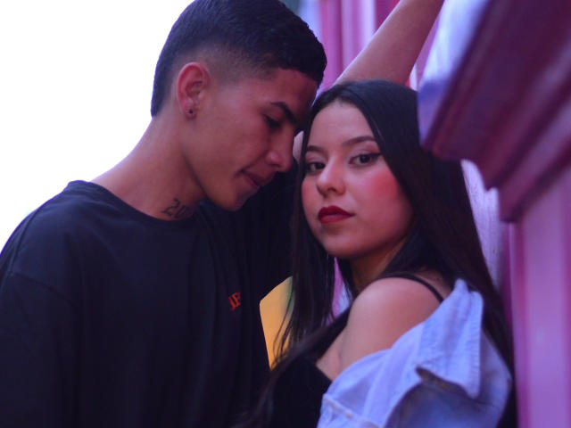 KylieAndJustin, a cute couple, standing close. Kylie has long dark hair, red lipstick, and a denim jacket. Justin, with short black hair and a tattoo, leans in.