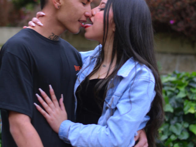 KylieAndJustin with long black hair, tongue out, kissing a tattooed Asian dude in a black shirt. She's in a blue denim jacket, hand on his chest. Boob touch.