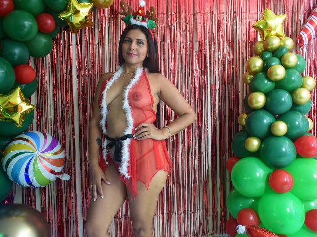 KatyaMore staat in een kerstthema ingerichte setting, gekleed in rode, doorschijnende lingerie met witte bontrand, waarbij haar kleine, stevige borsten en platte, kale billen zichtbaar zijn. Ze heeft donker haar..