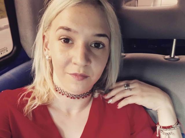 CataleyaHotty69, avec des cheveux blonds, un t-shirt rouge, un collier, une bague et un bracelet, assise dans une voiture, regardant la caméra, souriant, montrant ses seins, mignonne, éclairage doux..