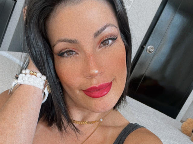 Liliysweet ha i capelli neri, un rossetto rosso e gli occhi marroni. Indossa un braccialetto bianco e una collana dorata, e sorride con una mano sulla testa..