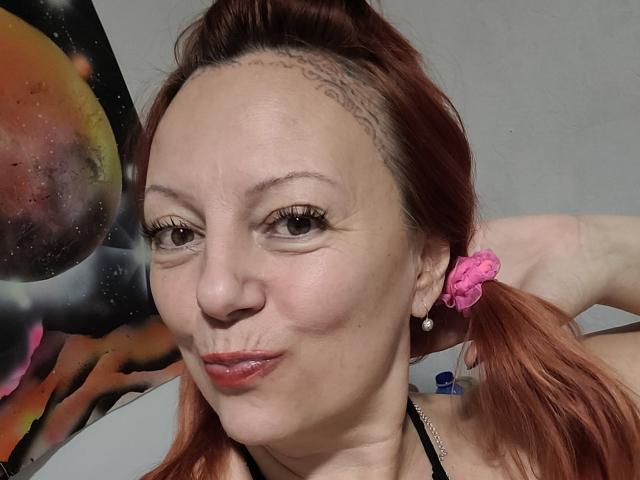 BarbaraBowie tiene la piel clara, coletas rojas con hebillas rosas, y una trenza en la frente. Está haciendo una mueca con los labios rojos ligeramente entreabiertos. Sus ojos son marrones..