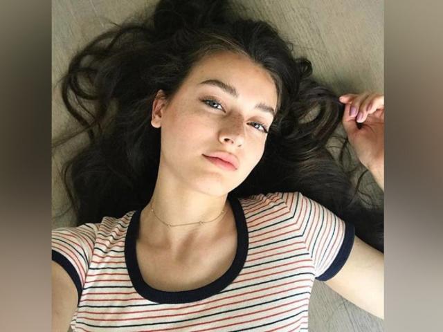 BabeJoelle lying on a couch, wearing a striped shirt, with long dark hair spread out, brown eyes, and a slight smile, looking relaxed and cute.