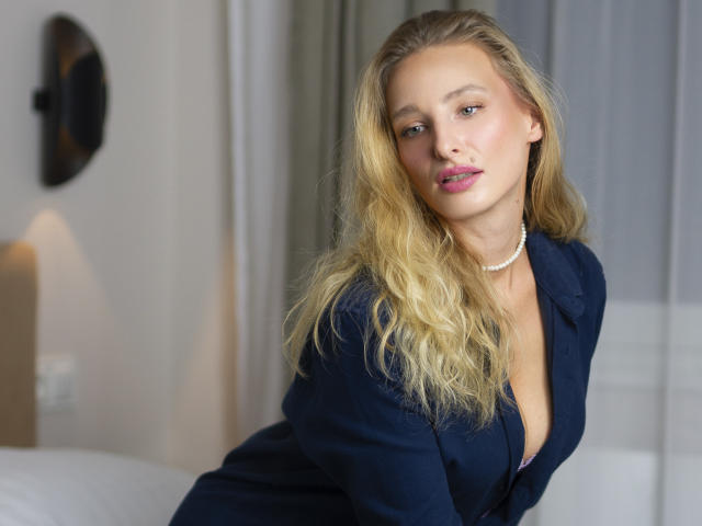 Marilyn: Cabelos loiros, camisa azul de botões, colar de pérolas, batom rosa, camisa ligeiramente aberta mostrando o colo, inclinada para frente, olhando para a câmera com um sorriso sutil e sexy..