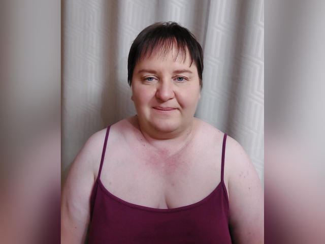 LimonkaFire, una mujer corpulenta con cabello corto y negro, vestida con un top morado de tirantes finos, sonriendo suavemente a la cámara. Tiene piel clara y senos pequeños..