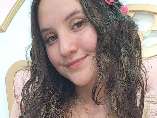 ChloeDulce has wavy brown hair, light skin, and a small nose with a gentle smile. She's wearing a pink hair clip and has subtle makeup.