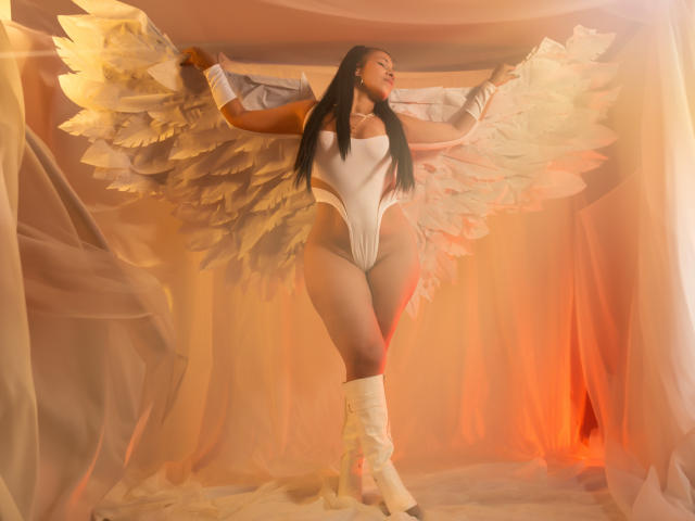 LaurenHills with large white angel wings, wearing a tight white one-piece, long black hair, white boots, standing, arms raised, soft orange and white light, looking up.