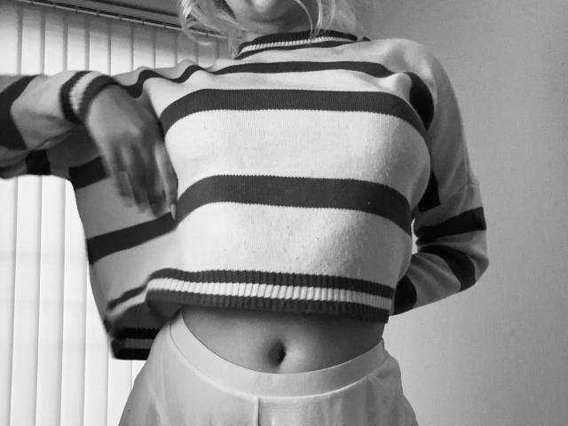 SugarrX indossa un maglione a righe, alzandolo per rivelare un ventre piatto e liscio, con un ombelico ben visibile. Il seno è coperto dal maglione. Foto in bianco e nero..