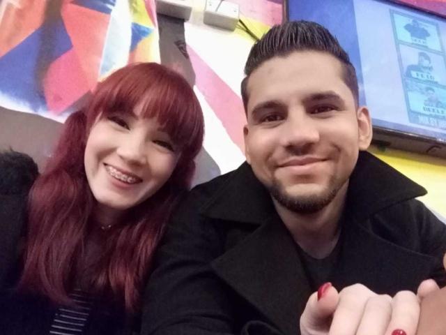 AkemixDiego mit roten Haaren und Pony, lächelnd, neben AkemixDiego mit kurzen schwarzen Haaren und Bart, der einen schwarzen Mantel trägt, beide auf einem Selfie, wobei rote Nägel zu sehen sind..