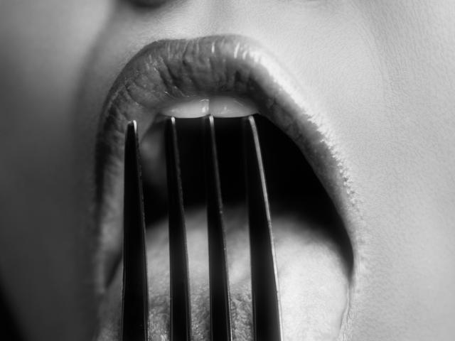 La bouche de Maisy Warner est grande ouverte, ses bagues dentaires en métal apparent, sa langue et ses lèvres brillantes visibles dans une photographie en noir et blanc, très détaillée et en gros plan..