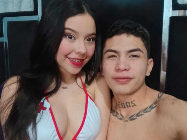 KylieAndJustin with long black hair, red lipstick, white bikini with red trim, and small tits, standing next to Justin with short black hair, shirtless, tattooed neck, and small ass.