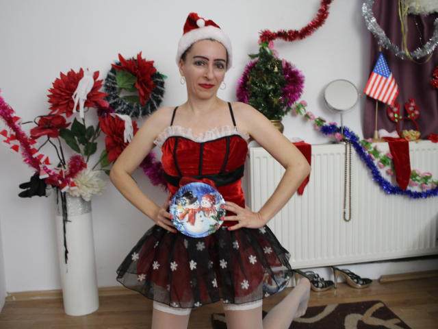 EvelynAngel wearing a red velvet corset with black lace, white frill, black star-patterned skirt, and Santa hat, holding a plate with a winter scene, has tits and a cute smile.