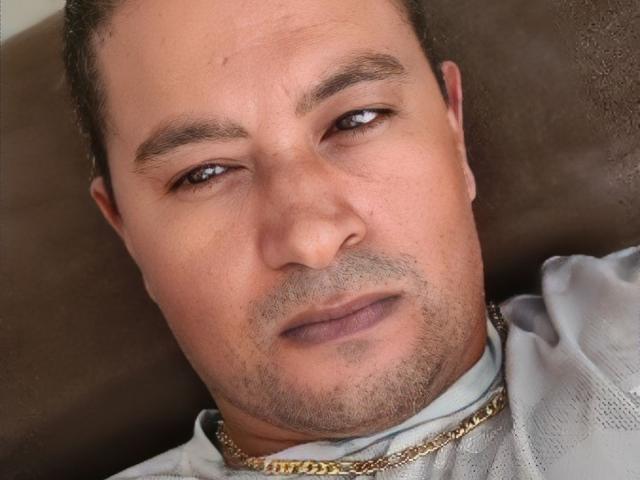 O Sr. BlackHot tem um rosto gordinho, com olhos castanhos, cabelo curto e escuro, pele clara e uma barba discreta. Ele está usando uma corrente de ouro e uma camisa cinza..