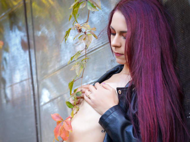 CindeFunRella with purple hair, holding a vine with pink flowers, wearing a black leather jacket, covering her small tits with her hands, looking down with a soft expression.