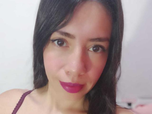 AnyJhonsHentay ha gli occhi marrone scuro, i capelli lunghi neri e il rossetto rosa con un velo di rossetto viola sopra. Sorride dolcemente, indossando una maglia di pizzo viola..