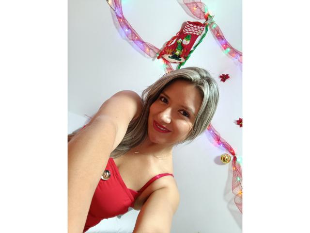 ValeriaHunter69 with gray hair, red bra, smiling down, showing small boobs, cute face, pink lipstick, fair skin, Christmas decorations in background, selfie from below.